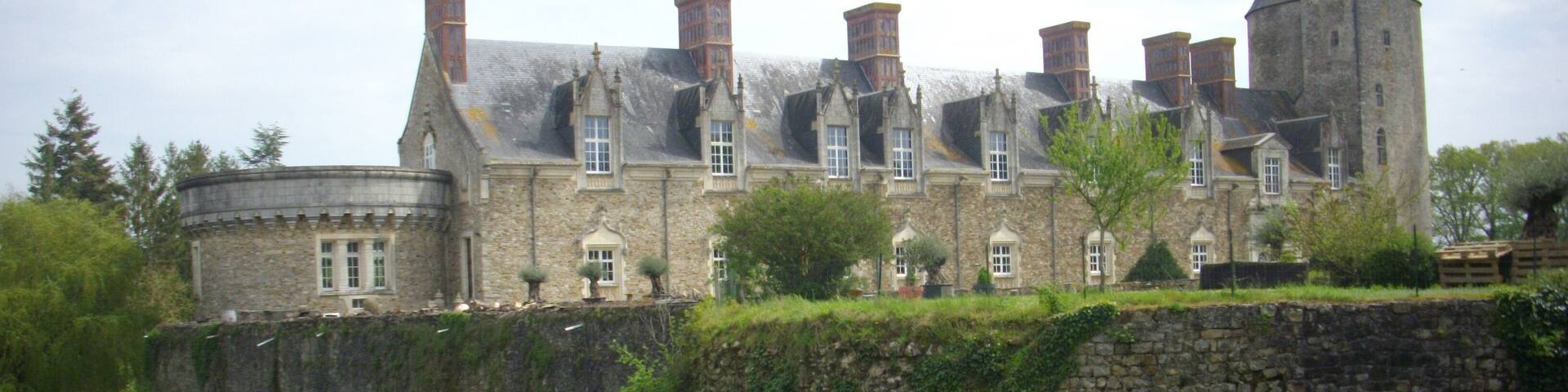 A historic stone castle with multiple chimneys, surrounded by lush greenery and a stone wall.