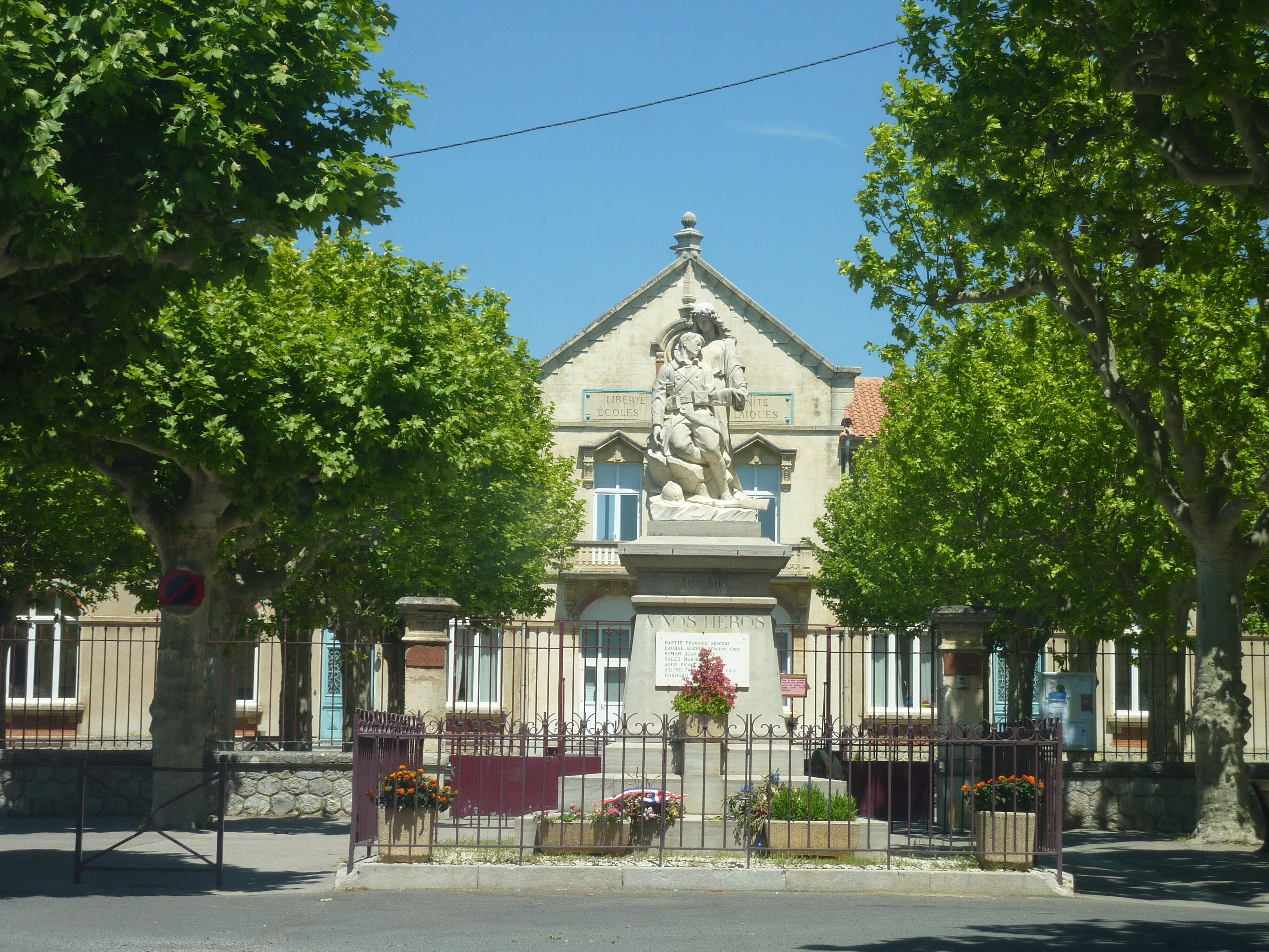 A building with a statue of a soldier on a pedestal, surrounded by trees and a fence with flower boxes.