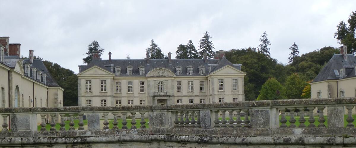 A large, historic building with a symmetrical facade, surrounded by a stone wall and lush green lawn.