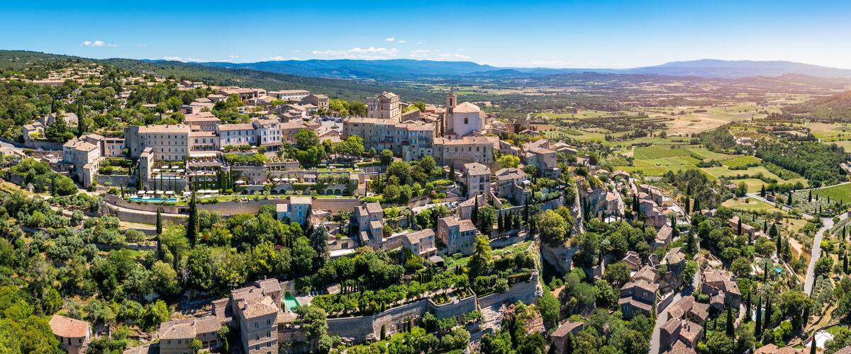 A historic town with medieval architecture, terraced vineyards, and a mountainous backdrop.
