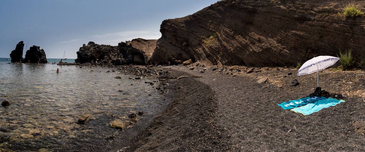 A rocky beach with a clear sky, a large rock formation, and a beach umbrella.