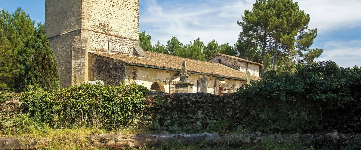 A historic stone tower with a tiled roof, surrounded by lush greenery and trees.