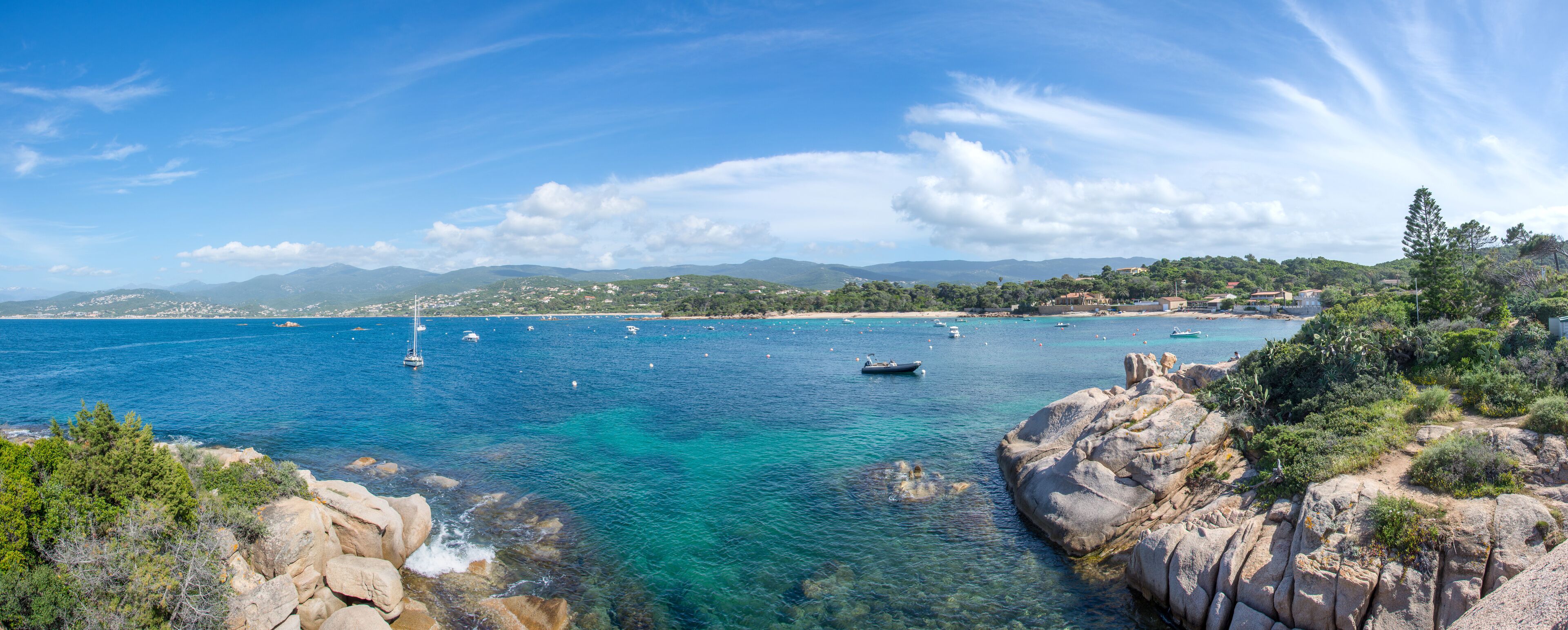 A coastal landscape with clear blue waters, rocky shores, and distant mountains.