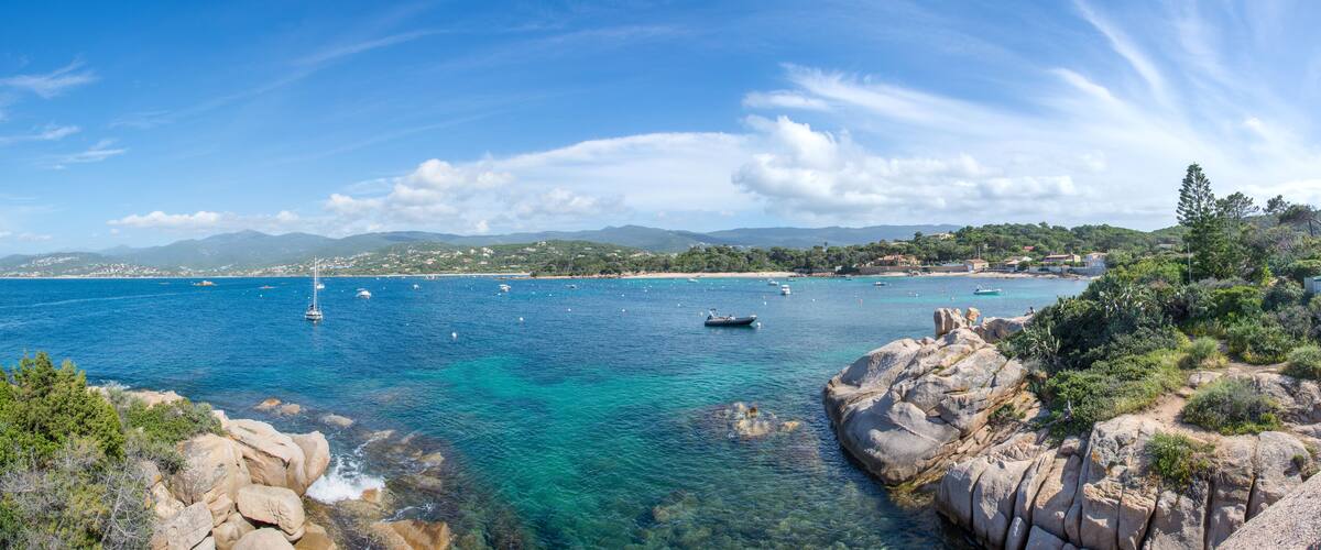 A coastal landscape with clear blue waters, rocky shores, and distant mountains.