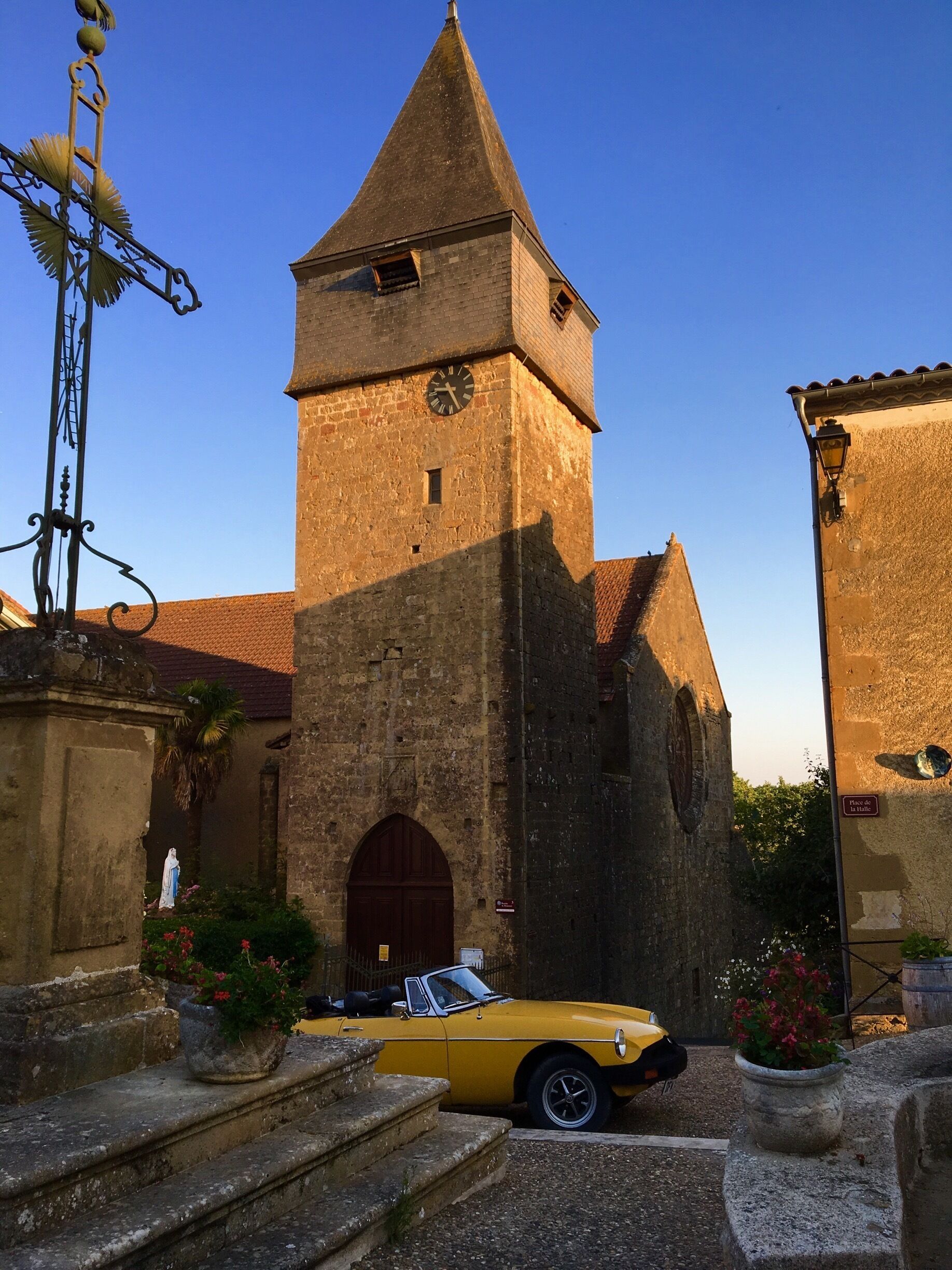 A historic church with a bell tower, a yellow convertible parked in front, and a weather vane.