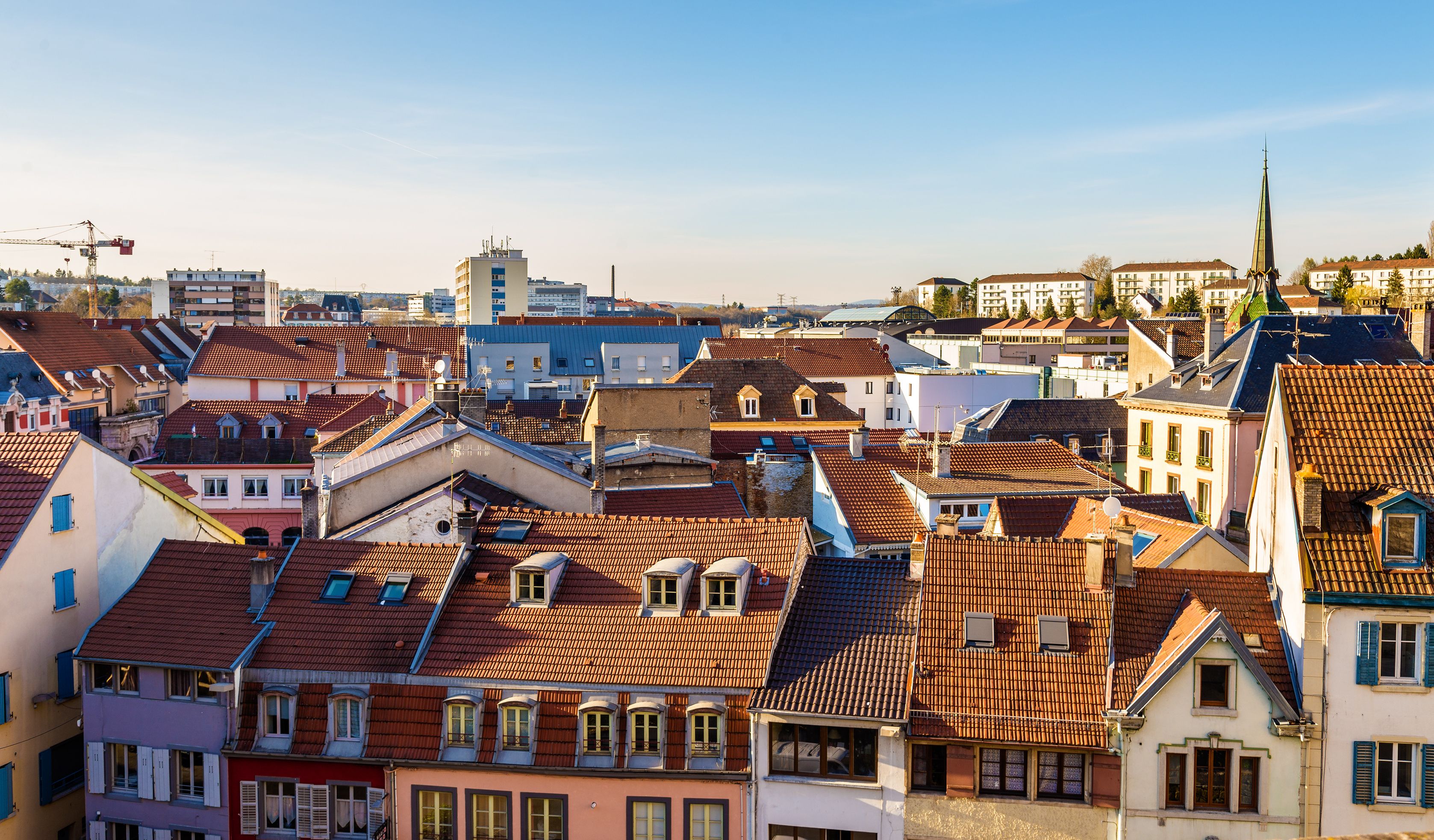 Ein dicht bebautes Stadtgebiet mit verschiedenen Gebäuden, darunter Wohnhäuser mit roten Ziegeldächern und einem markanten Kirchturm.