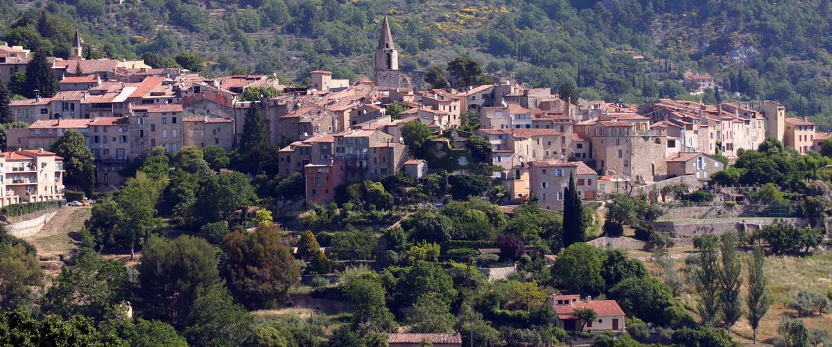 A historic town with red-roofed buildings nestled in a valley surrounded by lush greenery and hills.