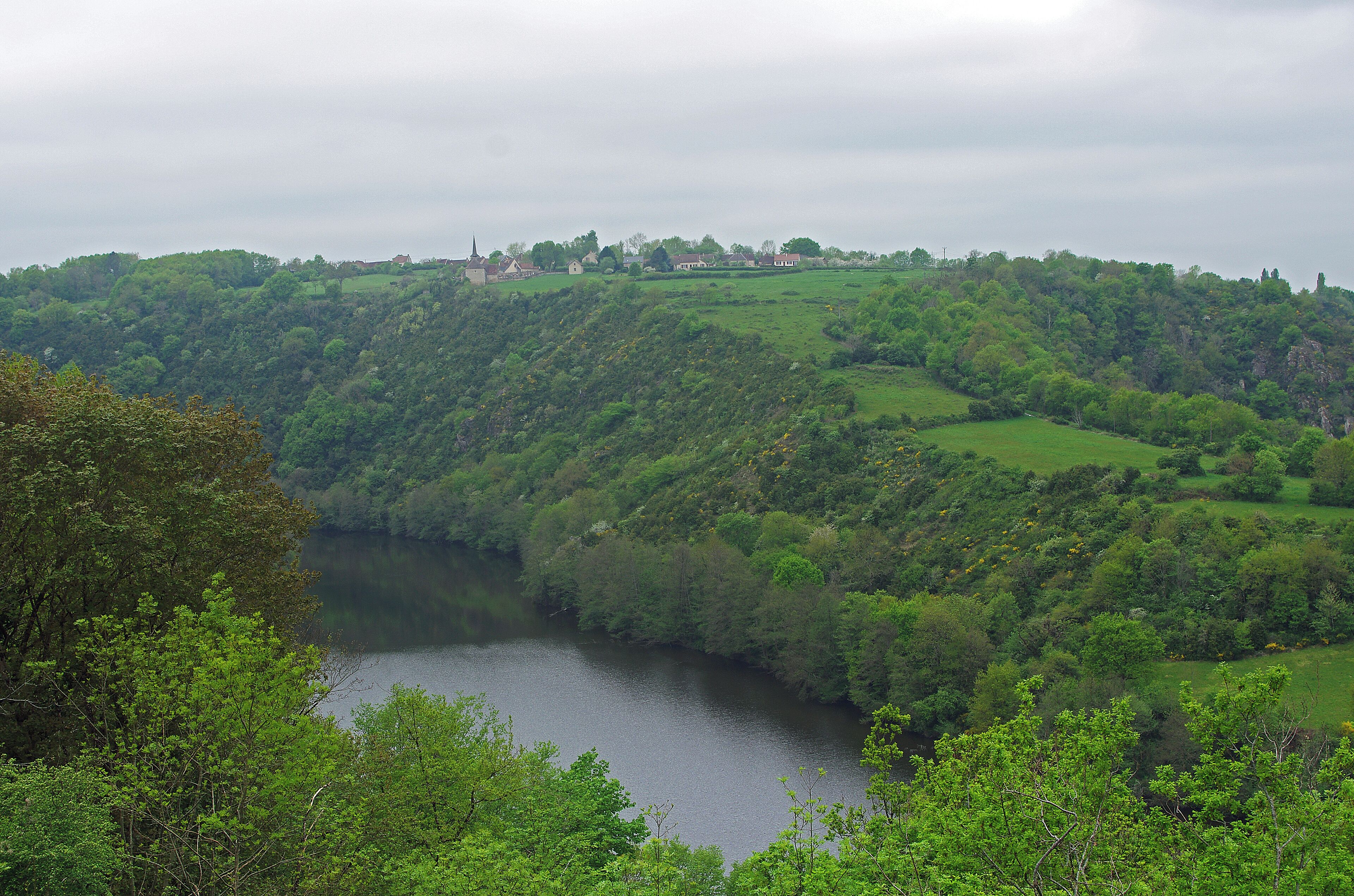 A river winding through a lush valley with rolling hills and scattered houses.