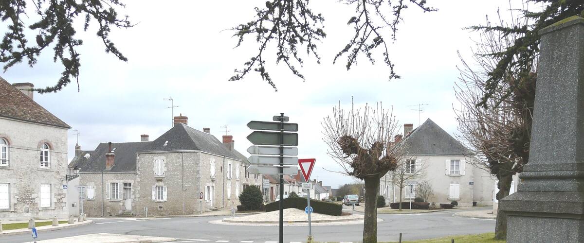 A rural intersection with stone buildings, a yield sign, and a chain-locked bollard.