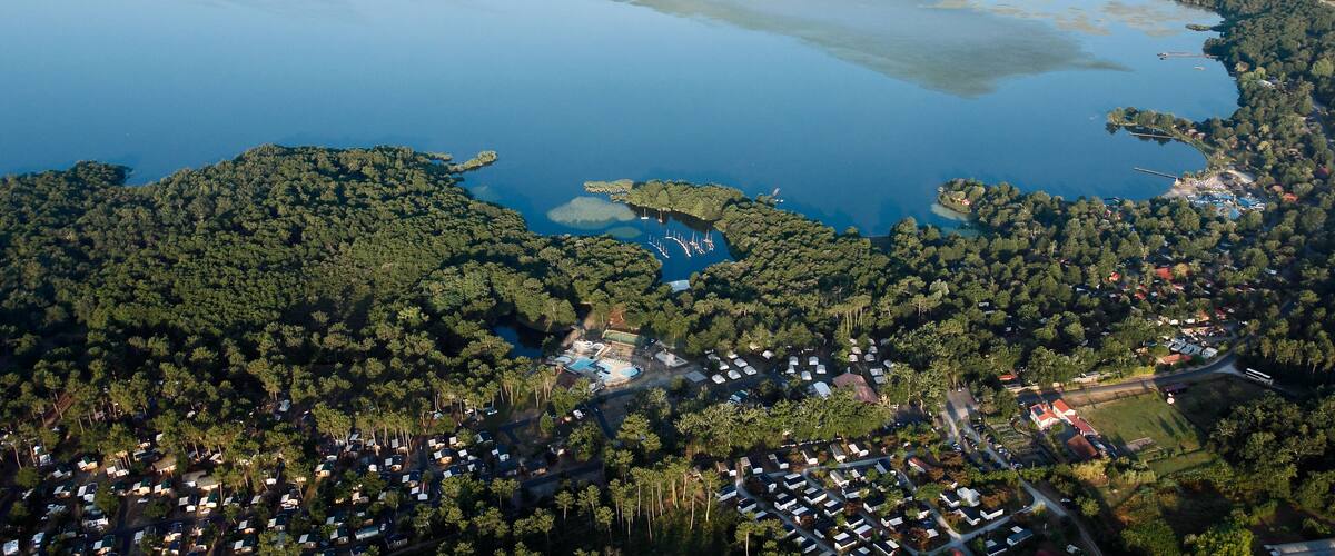 An aerial view of a lake surrounded by dense forests and a small town with visible buildings and roads.