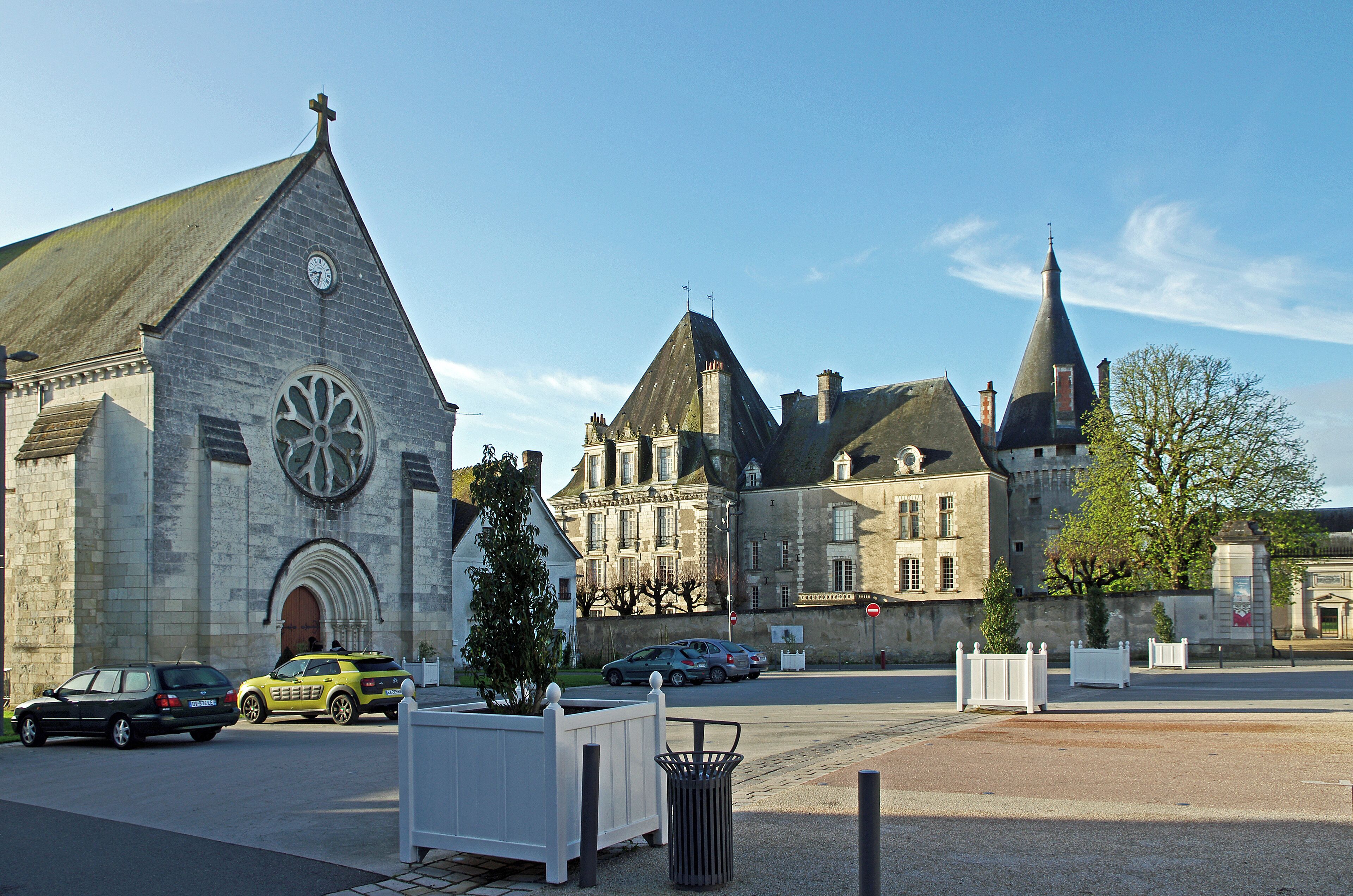 A church with a clock tower and a large window, a stone building with a pointed roof, and a street with cars and a white fence.