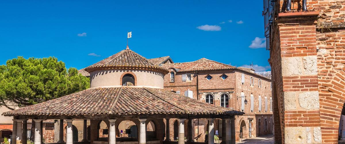 A historic building with a tiled roof and a central dome, surrounded by a cobblestone courtyard with arches.