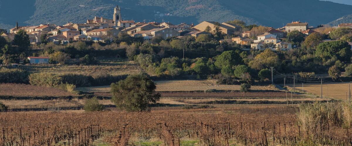 A village with a prominent church tower, surrounded by vineyards and hills.