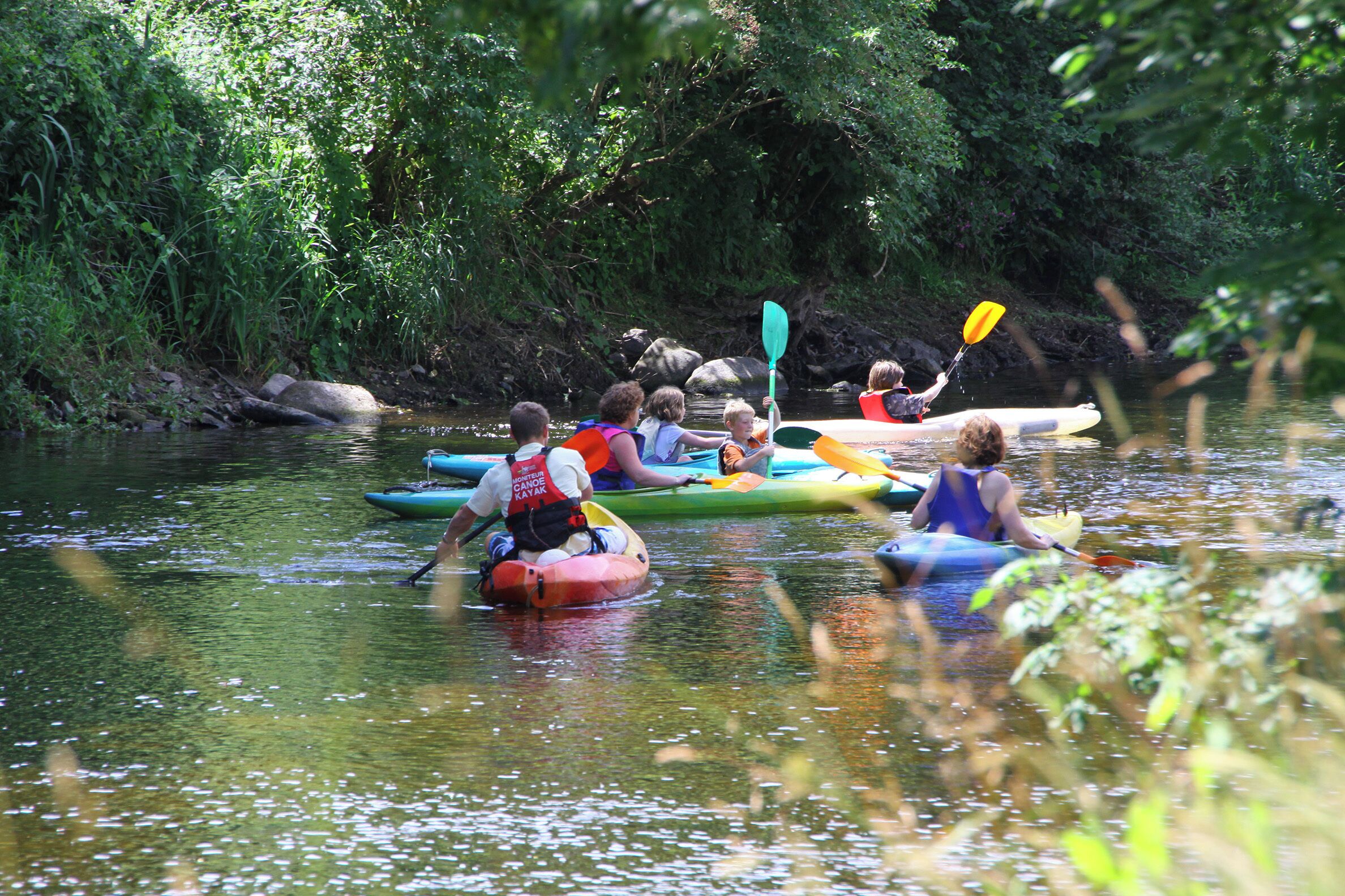 People kayaking on a calm river surrounded by lush greenery.