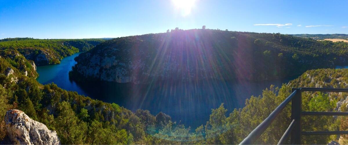 A mountainous landscape with a river, a sunlit sky, and a metal railing.