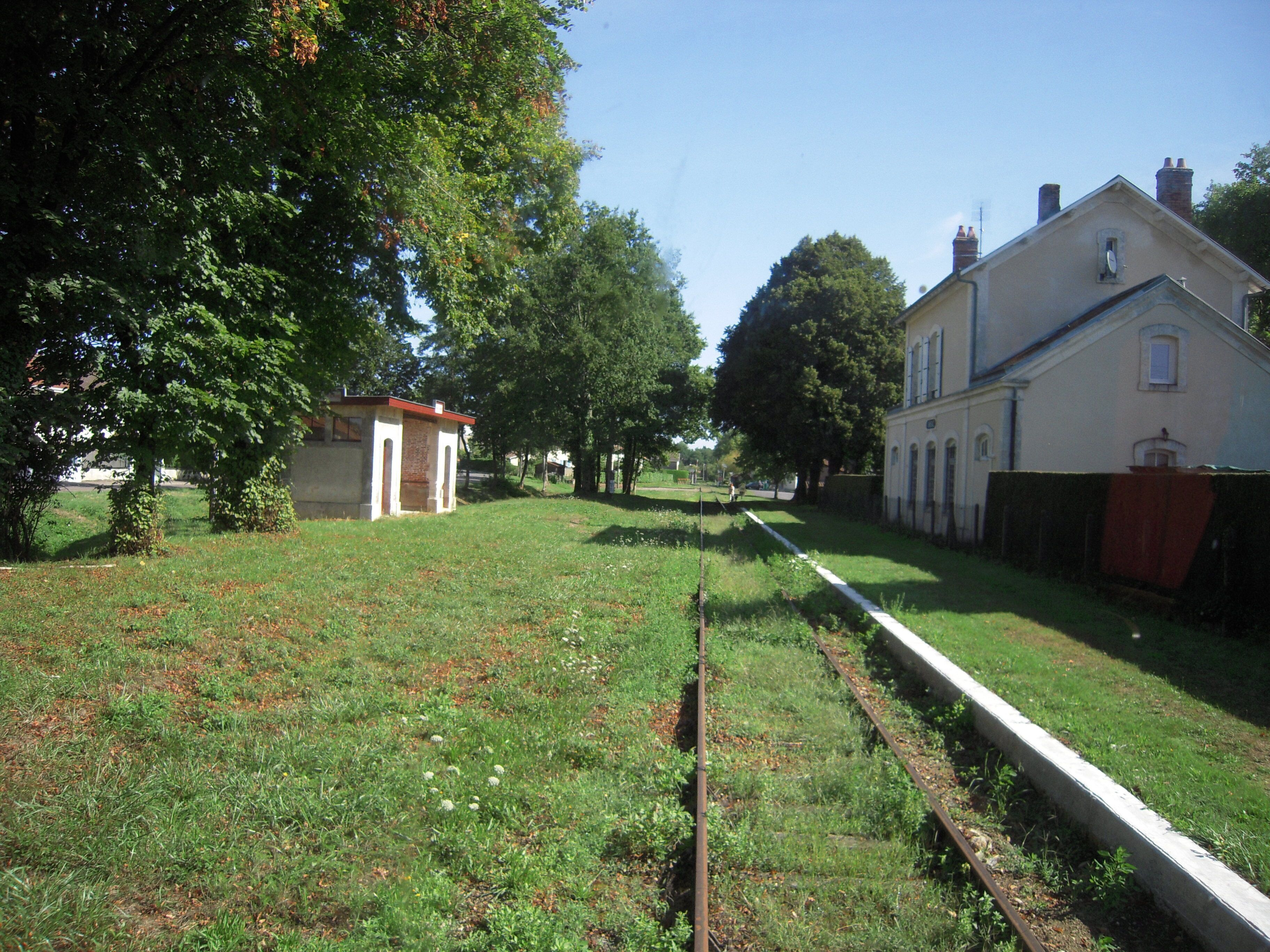 A grassy area with a small building, trees, and a large house.