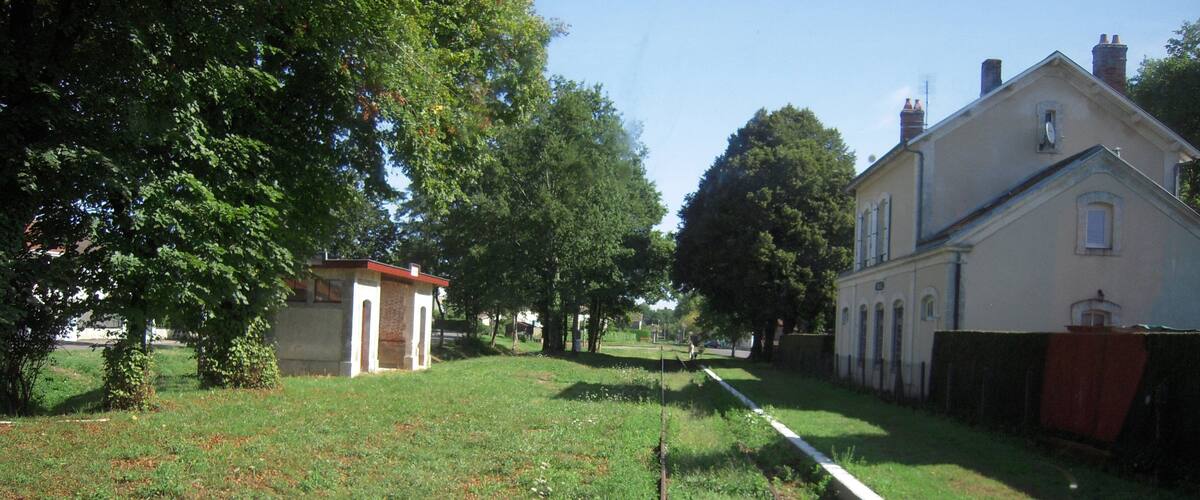 A grassy area with a small building, trees, and a large house.