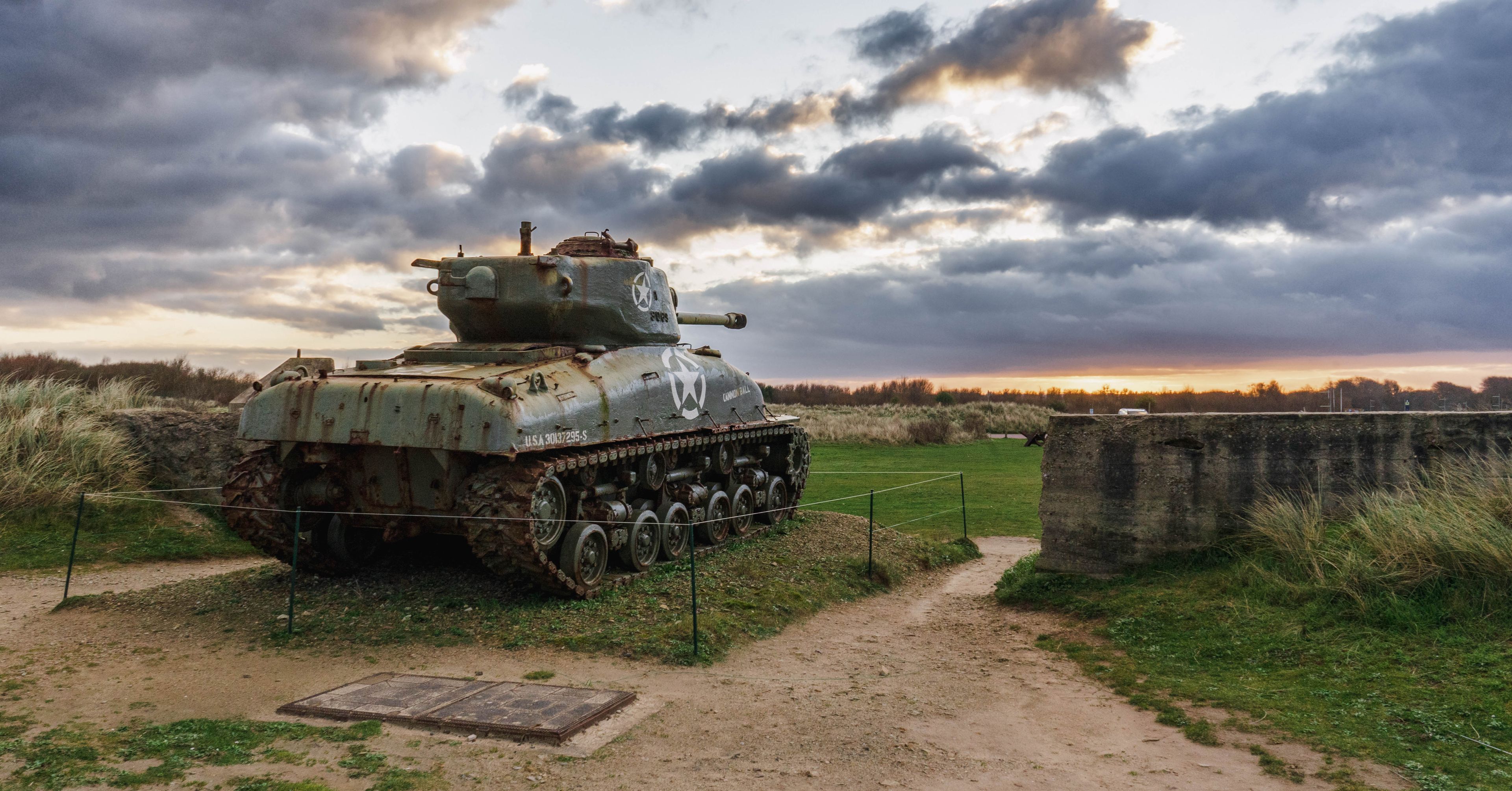 Un char d’assaut est exposé dans un champ verdoyant, avec un ciel nuageux en arrière-plan.