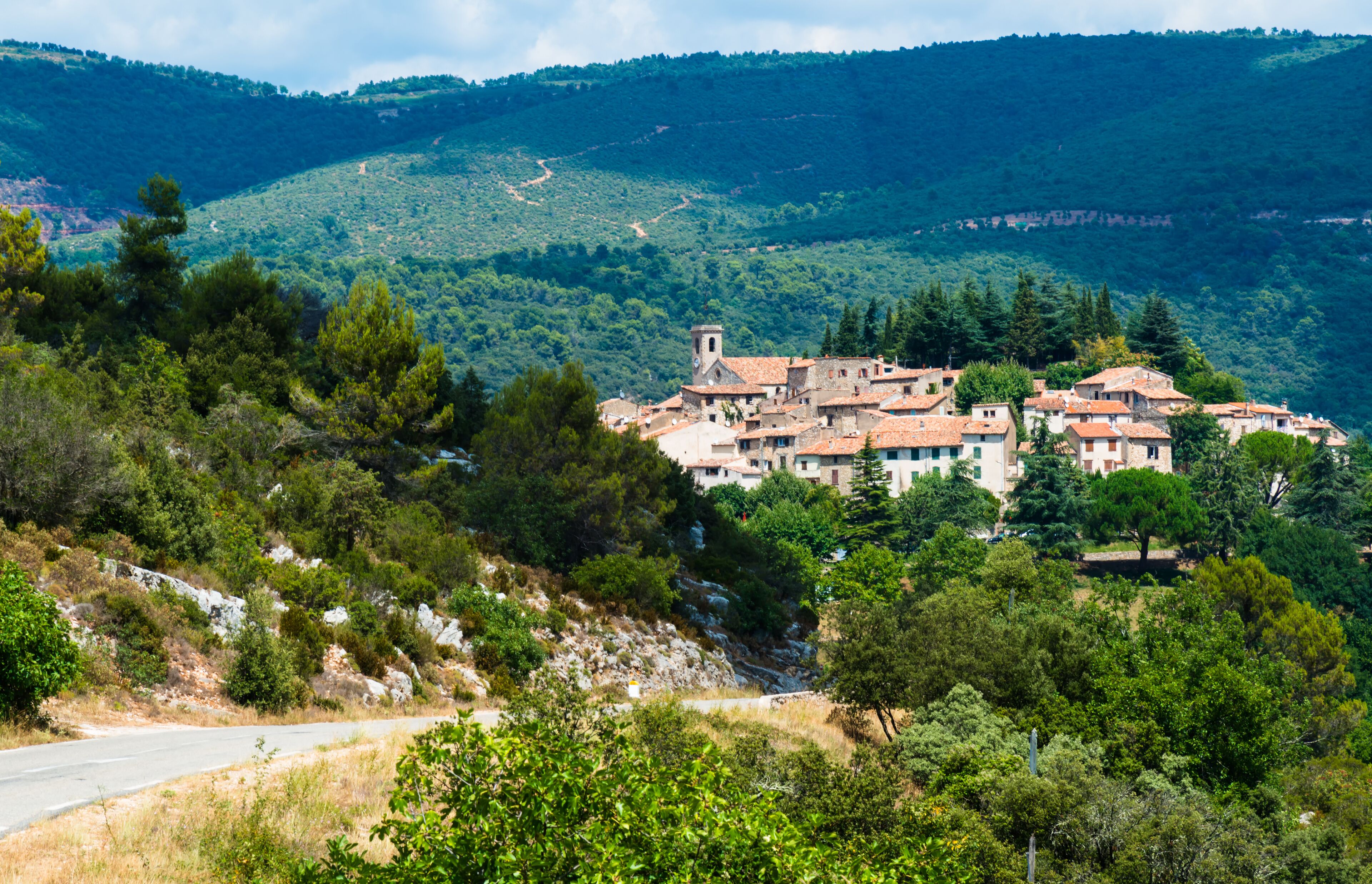 A hillside village with terracotta-roofed buildings, surrounded by dense forest and rocky terrain.