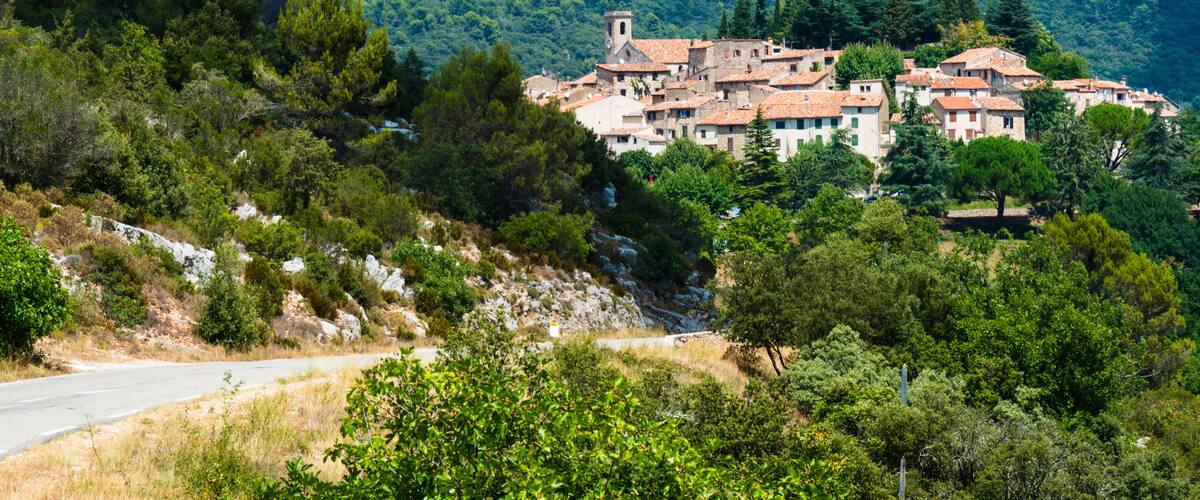 A hillside village with terracotta-roofed buildings, surrounded by dense forest and rocky terrain.