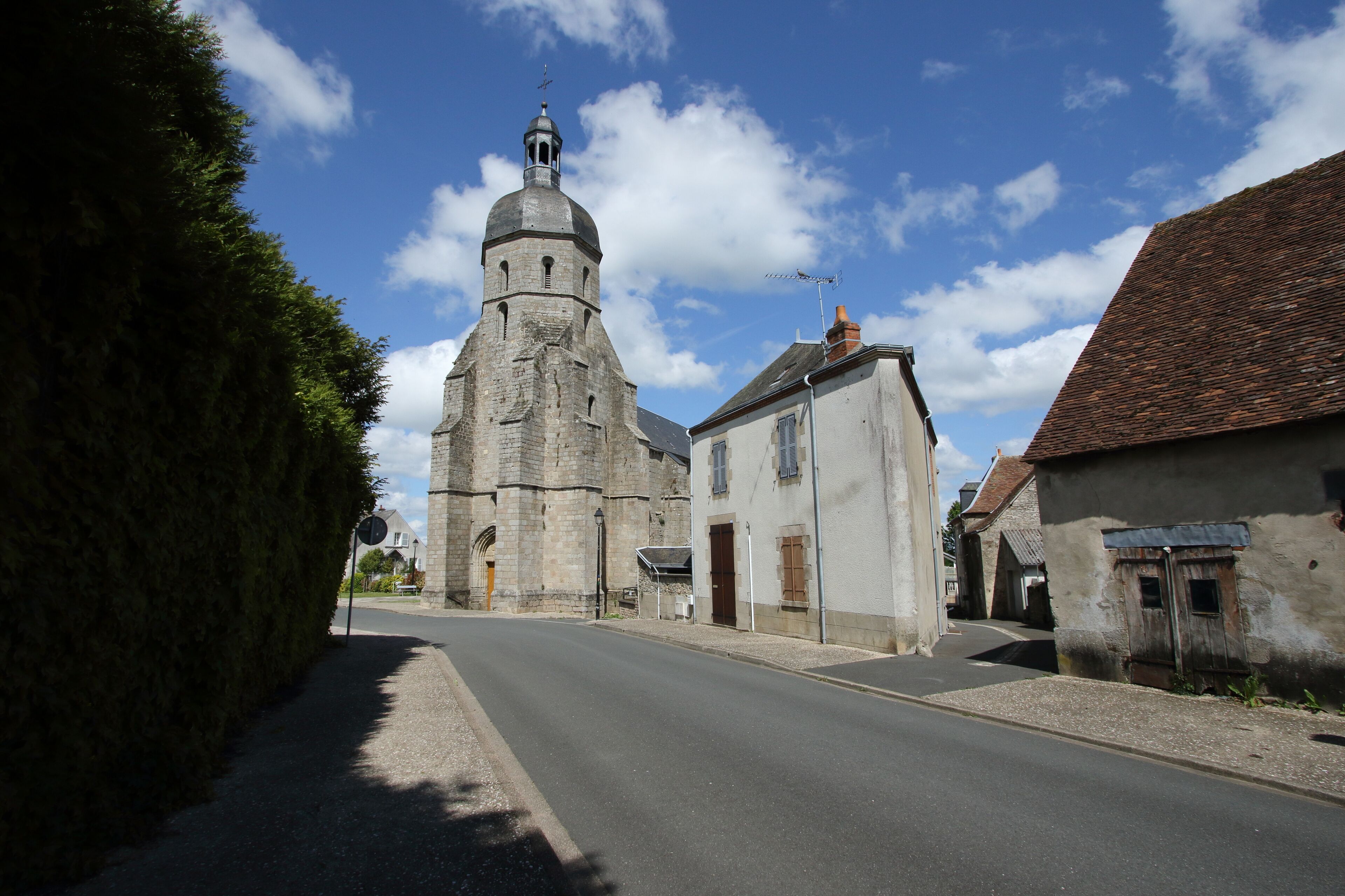 A historic church with a tall bell tower, a narrow street, and old buildings.