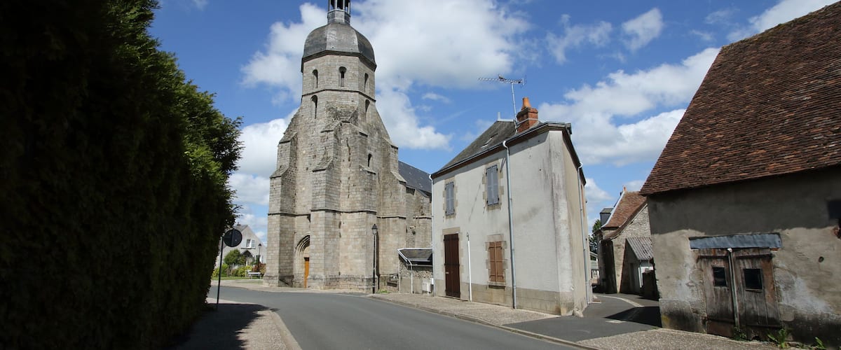 A historic church with a tall bell tower, a narrow street, and old buildings.