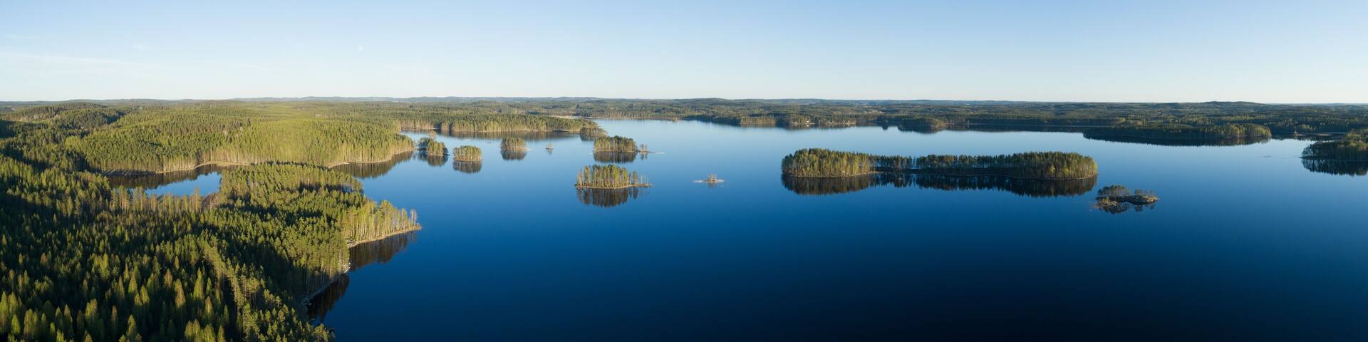 Aerial early clear summer day in finland with green forest, islands and blue water lakes and clear blue sky. Beautiful Finnish nature.