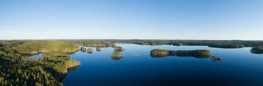 Aerial early clear summer day in finland with green forest, islands and blue water lakes and clear blue sky. Beautiful Finnish nature.