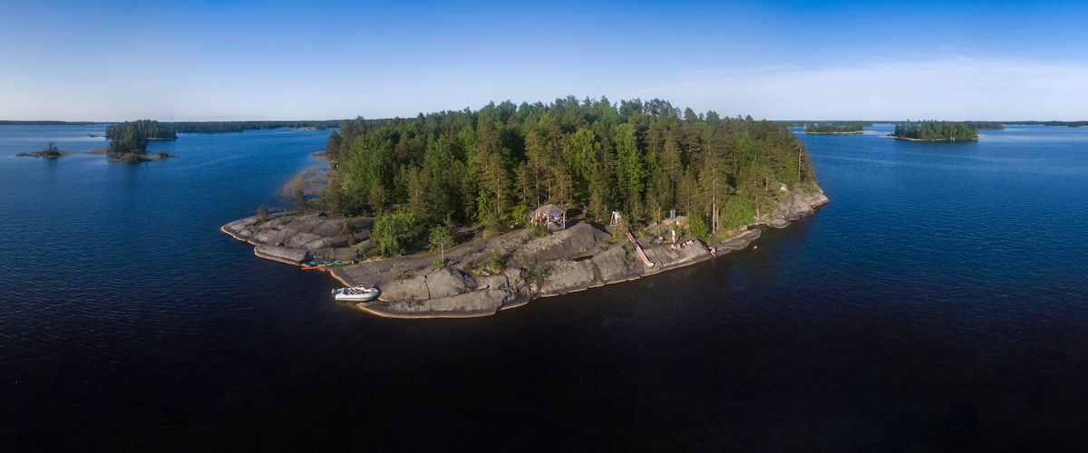 An aerial view of a forested island with a rocky shoreline, surrounded by calm water.
