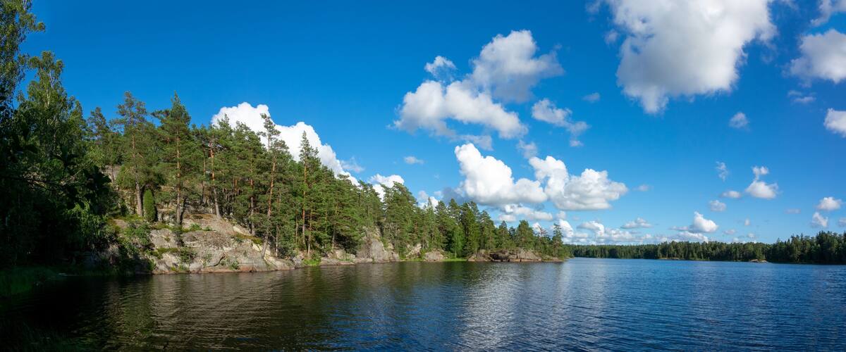 A calm lake surrounded by dense forest and rocky cliffs under a clear blue sky.