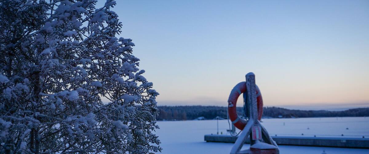 A snow-covered landscape with a lifebuoy sculpture and a dock in the background.