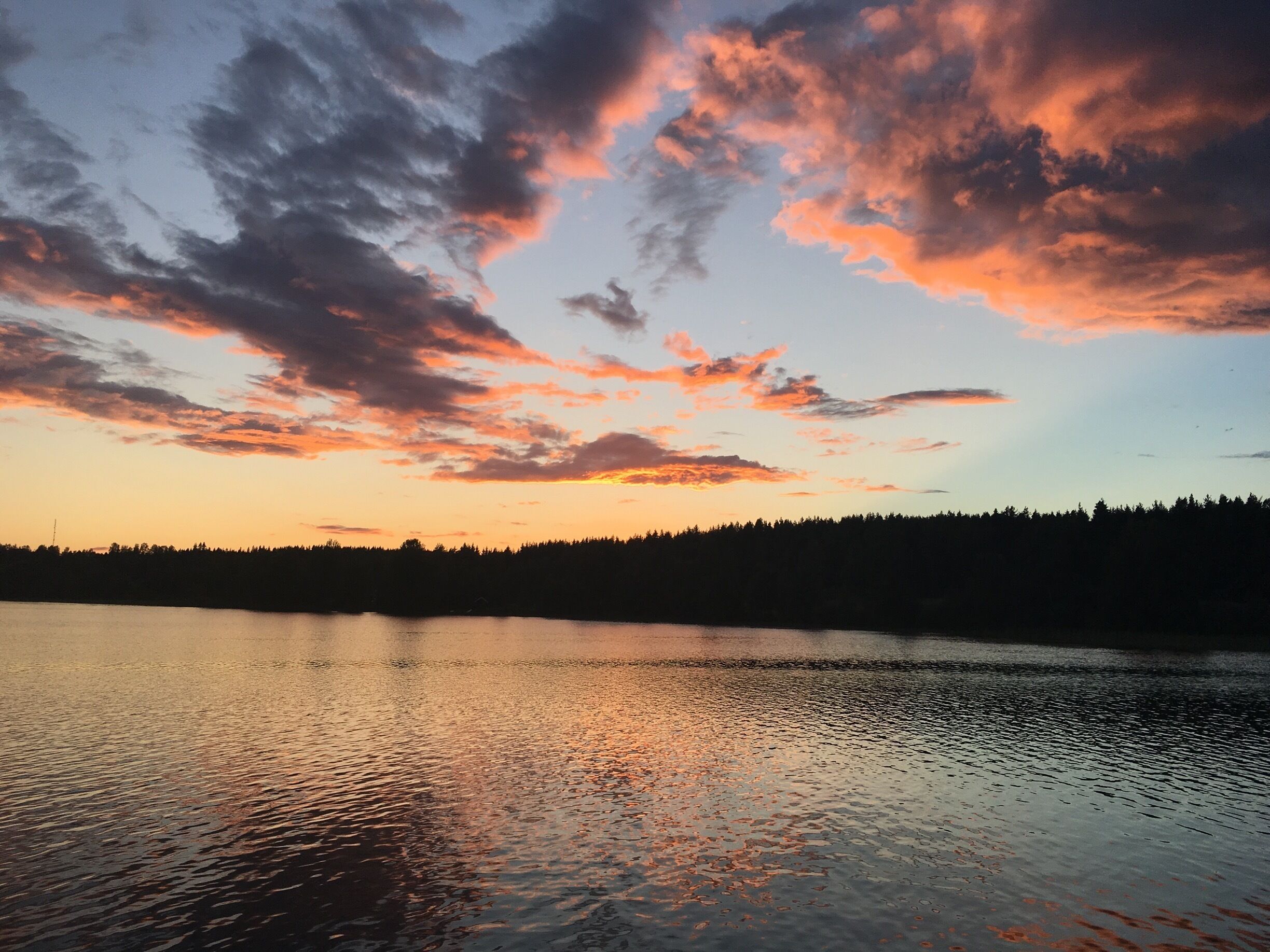 A sunset over a calm lake with a forested shoreline.