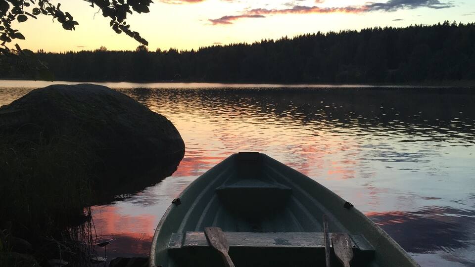 A rowboat by a calm lake at sunset with a forest in the background.