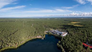Ilmakuva metsäisestä alueesta, jossa on järvi, suuri rakennus ja punakattoinen rakennelma.
