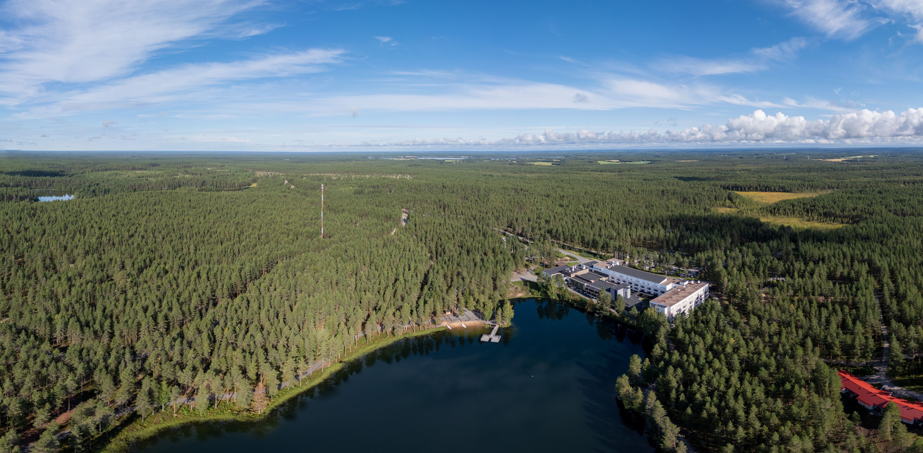 An aerial view of a forested area with a lake, a large building, and a red-roofed structure.