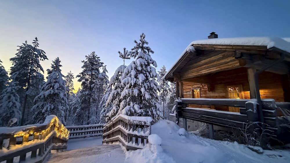 Snowy trees and illuminated wooden house in winter, evening mood, Oulanka National Park, Kuusamo, Finland