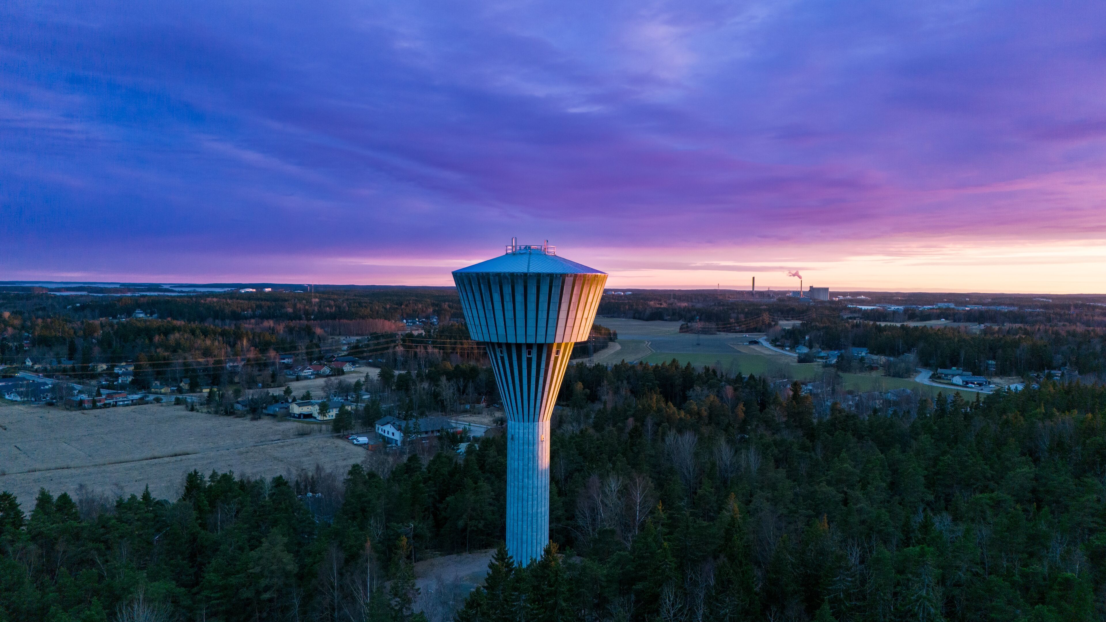 A water tower in a forested area with a sunset sky.
