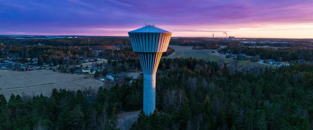 A water tower in a forested area with a sunset sky.