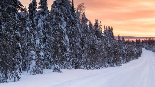 Icy snow covered winter road in the Arctic Circle at sunset in Lapland, Finland