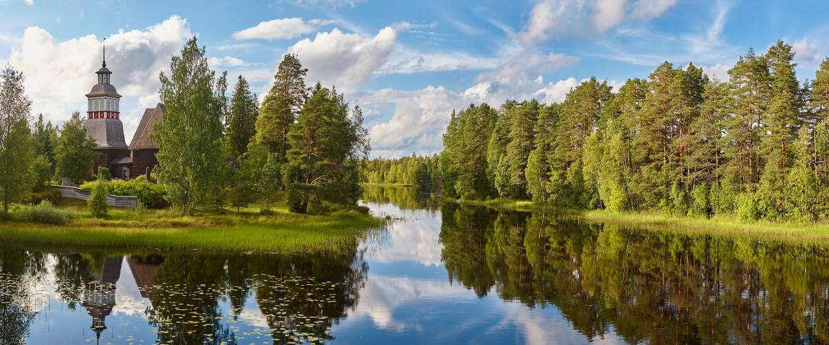 A serene landscape with a church, a calm lake, and a dense forest.