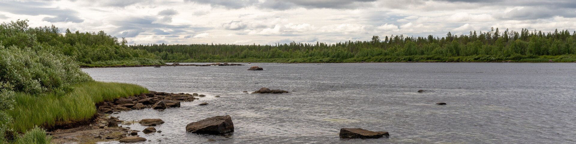 Un río con rocas y una orilla boscosa bajo un cielo nublado.