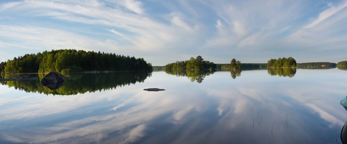 A calm lake with a boat docked on the right, surrounded by dense forest and clear skies.