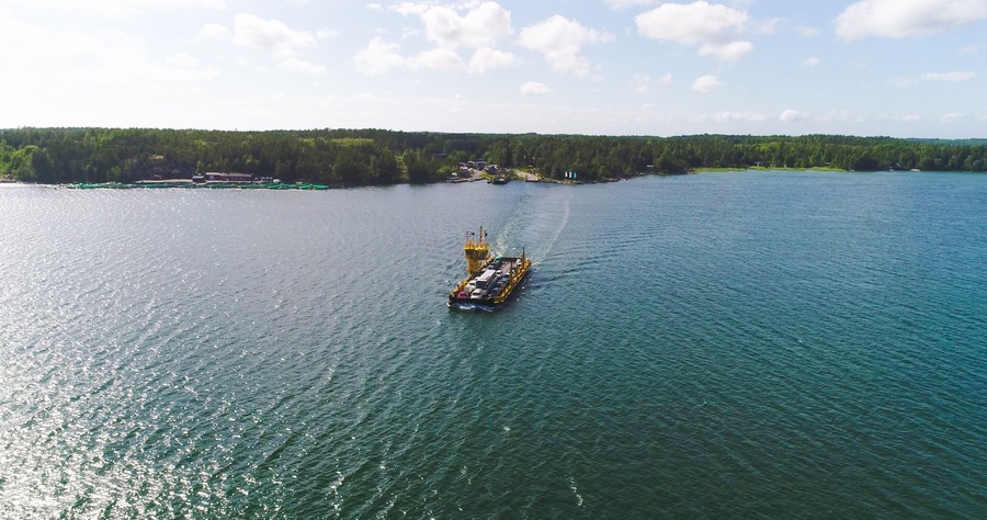 Rahtialus tyynellä järvellä, jonka rannalla on metsää.