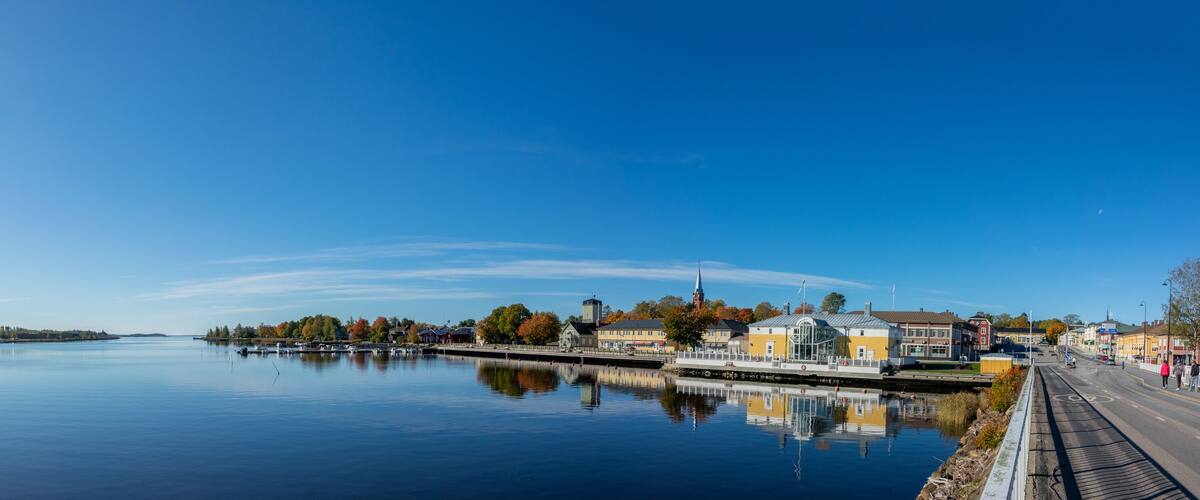 A calm lake with a fountain, a dock, and buildings along the shore.