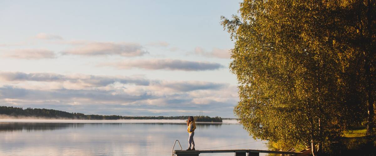 A calm lake with a dock extending into the water, surrounded by trees and a distant shoreline.