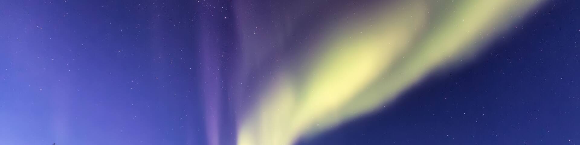 View of the ethereal aurora borealis paints the Arctic sky with vibrant green and purple hues above a snow-laden road, Karigasniemi, Lapland, Finland.