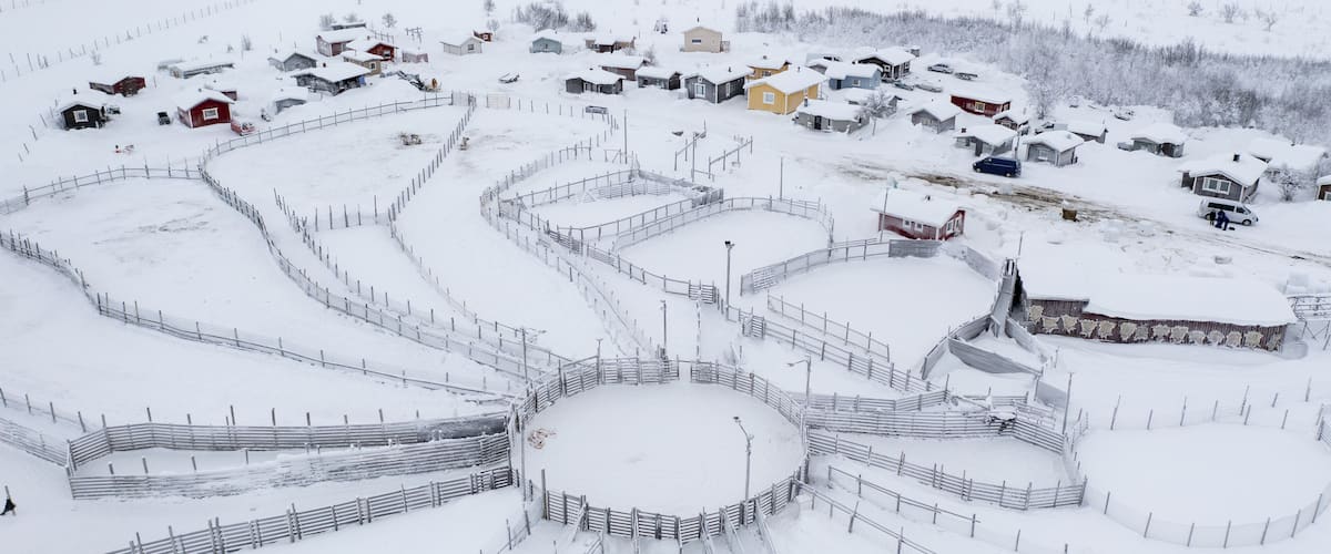 A snow-covered village with a circular layout of buildings and fences.