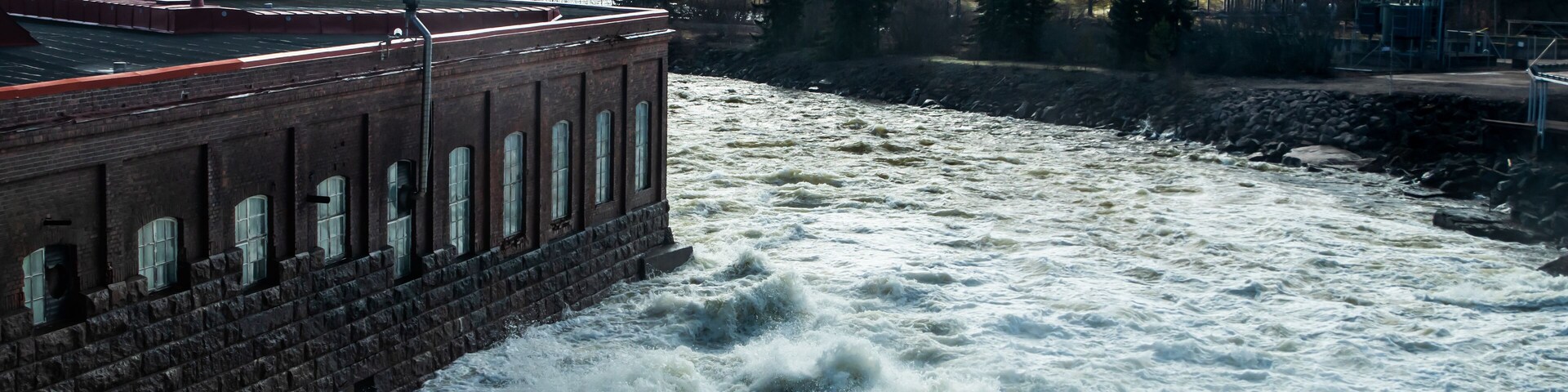 Un río con aguas turbulentas fluyendo cerca de un edificio de ladrillo.