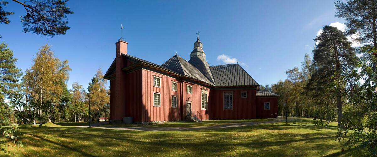 A red wooden church with a steeple and a large lawn in front.