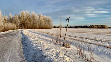 Een besneeuwde landweg die door een veld kronkelt, met een bord in de verte.